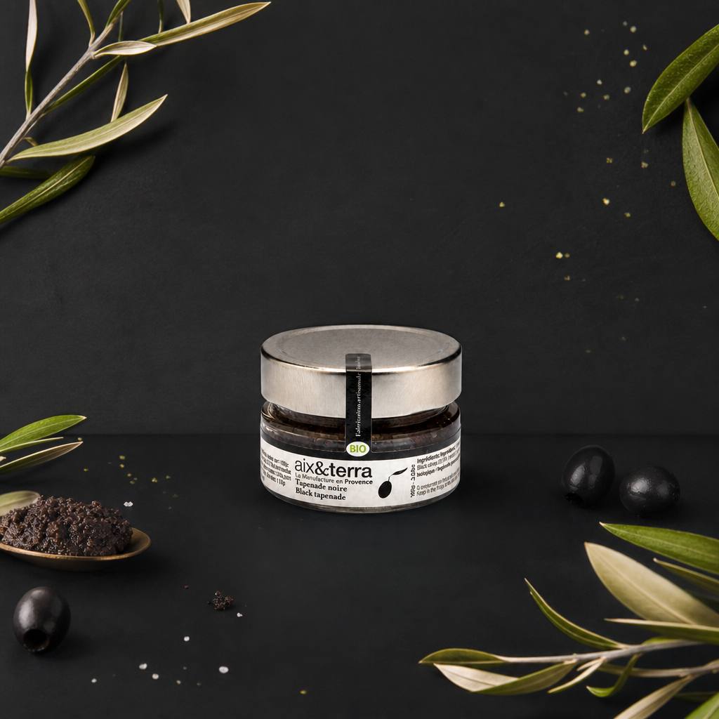 Pot de tapenade noire bio Aix & Terra présenté sur fond noir, entouré d’olives noires, de feuilles d’olivier et d’une cuillère garnie de tapenade, dans une ambiance élégante inspirée de la Provence.