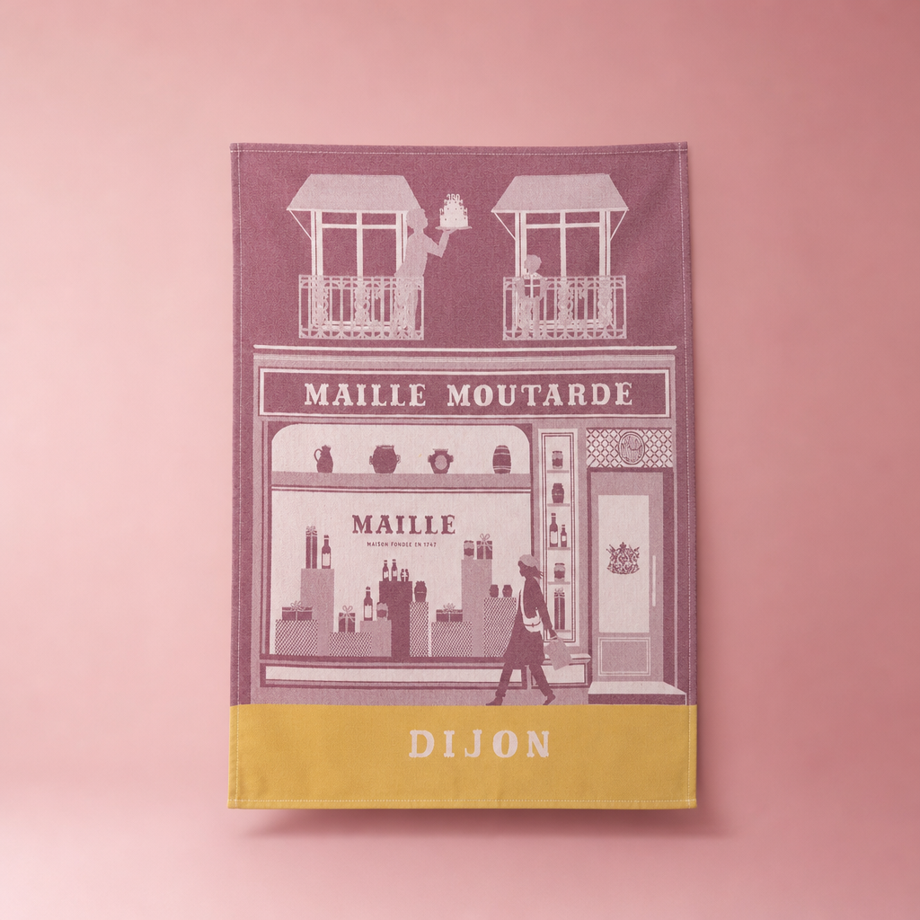 Torchon de cuisine Maille Dijon en coton jacquard, illustrant la façade emblématique de la boutique Maille sur un fond rose uni et élégant.