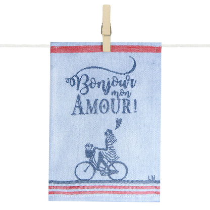 Para tapas de cuisine Maille illustré de l’inscription « Bonjour mon Amour ! » en bleu marine sur fond écru. Le visuel représente un personnage à vélo transportant une baguette et des fleurs dans un panier, encadré par des bandes rouges et bleues évoquant l’art de vivre à la française. Le torchon est présenté suspendu à une corde par une pince en bois.