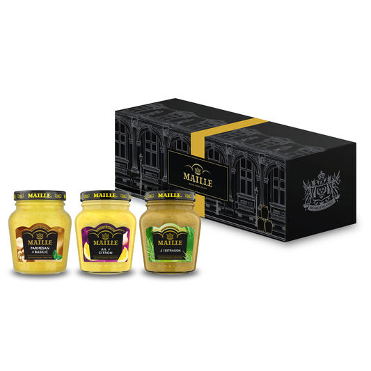 Coffret cadeau Maille composé de trois moutardes créatives présentées devant un élégant écrin noir décoré de motifs architecturaux et d’un ruban doré. La sélection comprend une moutarde Parmesan et Basilic, une moutarde Ail et Citron et une moutarde à l’Estragon, toutes présentées dans des pots en verre avec couvercle noir signature Maille. Le visuel met en avant une collection de saveurs raffinées inspirées de la gastronomie.